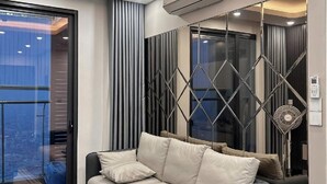 Una sala de estar moderna con un sofá, un ventanal de vidrio que da a un balcón y un aire acondicionado instalado en el techo.