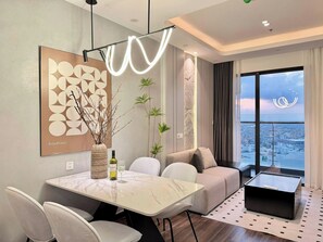 Een moderne woonkamer met een eethoek, een bank, een salontafel en uitzicht op de stad door grote ramen.