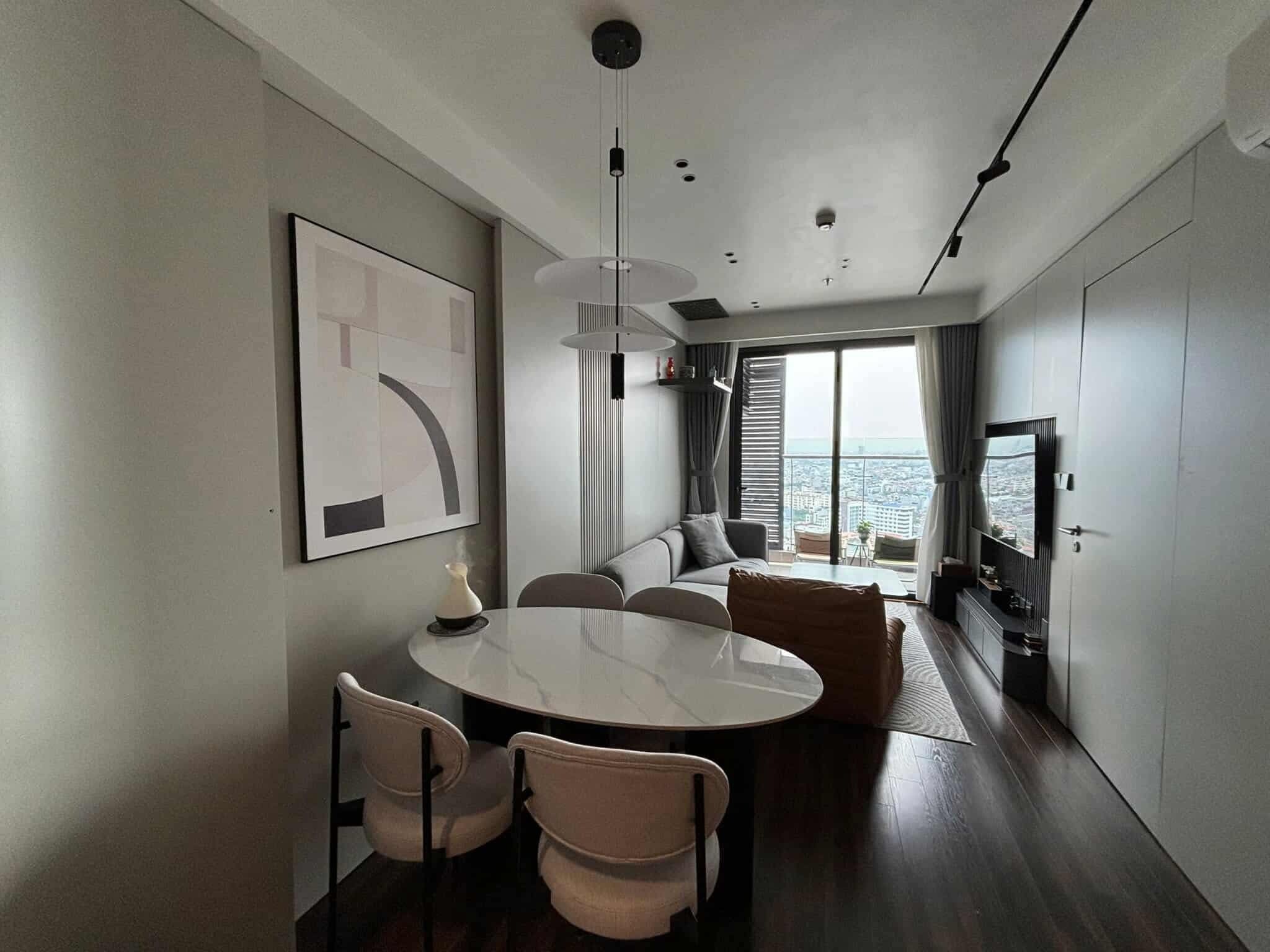 Een moderne woonkamer met een ronde eettafel, twee stoelen, een bank, een televisie en een groot raam met uitzicht op de stad.