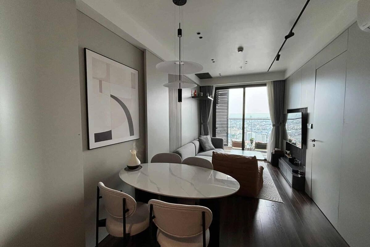 Ein modernes Wohnzimmer mit einem runden Esstisch, zwei Stühlen, einer Couch, einem Fernseher und einem großen Fenster mit Blick auf die Stadt.