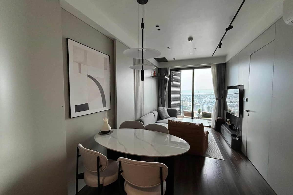A modern living room with a round dining table, two chairs, a sofa, a TV, and a large window with a city view.
