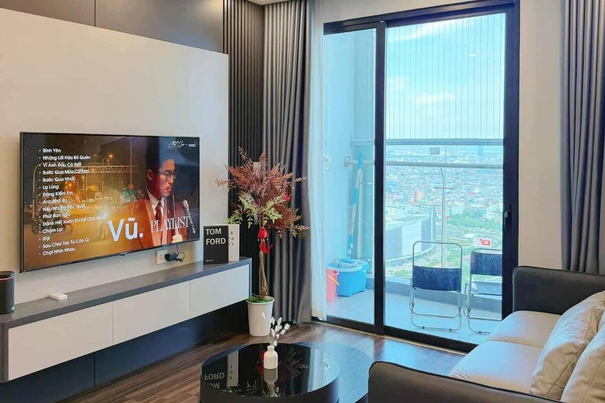 Ein modernes Wohnzimmer mit Fernseher, Couchtisch, Sofa und Blick auf die Stadt durch große Fenster.