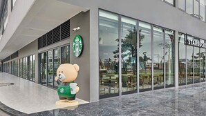 Una tienda Starbucks con una estatua de oso en el exterior, ventanas amplias y una fachada de edificio moderna.