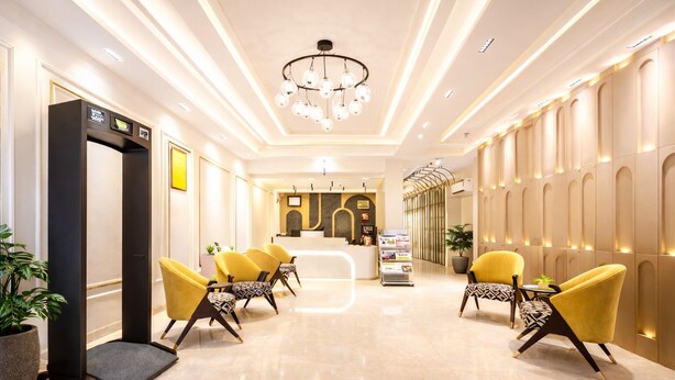 Un vestíbulo de hotel con una recepción, sillas amarillas, una araña y un diseño moderno.