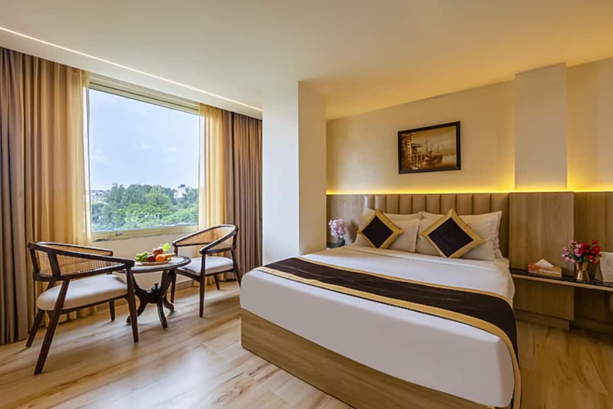 Habitación de hotel con una cama grande, dos sillas, una mesita con fruta y vistas a la vegetación por la ventana.
