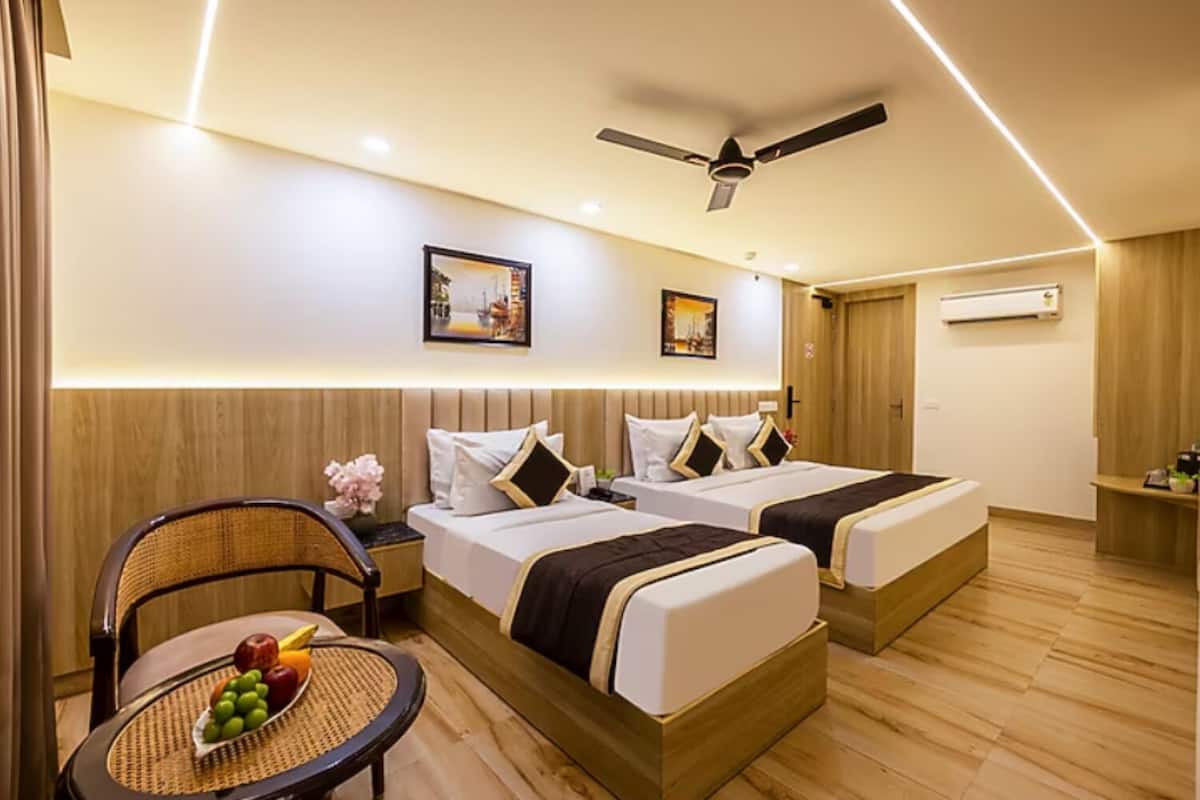 Habitación de hotel con dos camas, ventilador de techo, aire acondicionado de pared y una mesita con fruta.