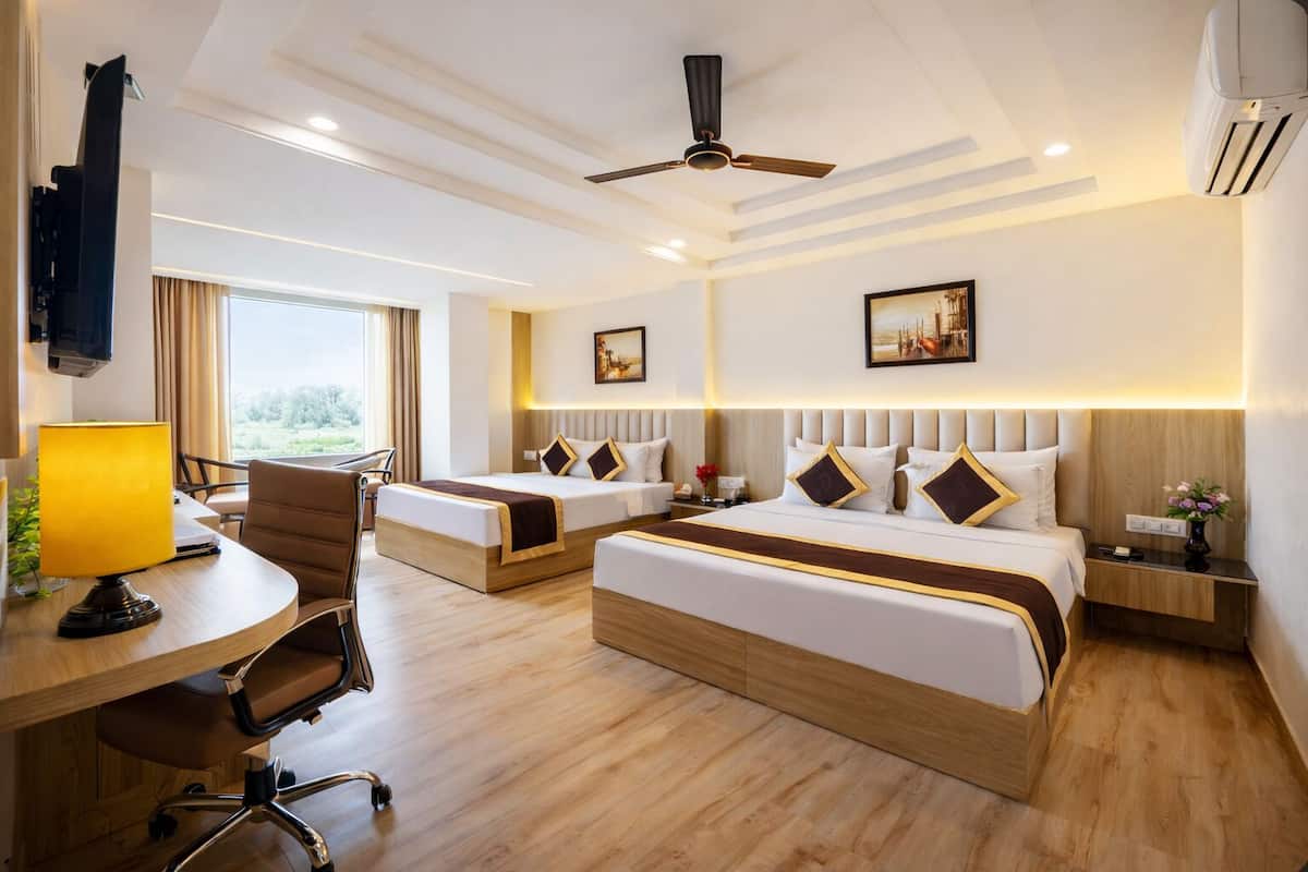 Habitación de hotel con dos camas, un escritorio, una silla, un ventilador de techo y obras de arte en las paredes.