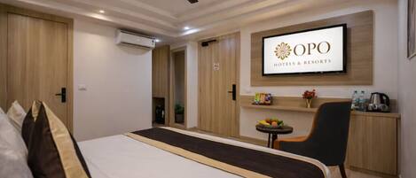 A hotel room with a bed, a desk, a chair, a TV mounted on the wall, and a ceiling fan.