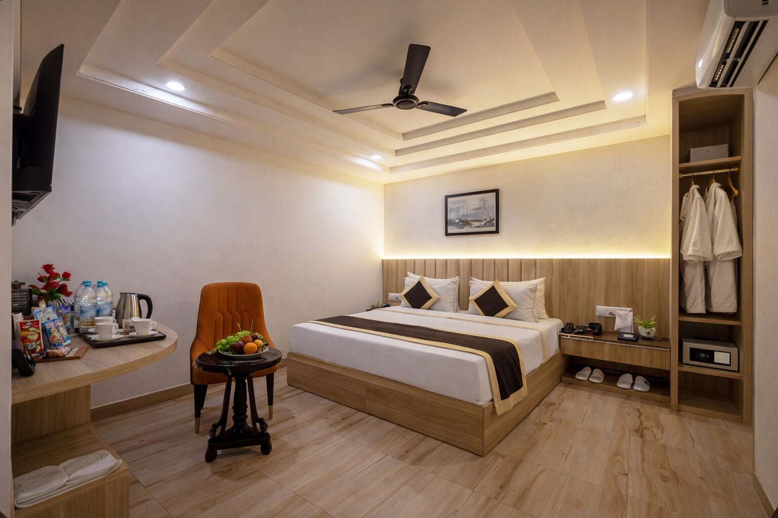 A hotel room with a bed, a desk with a chair, a small table with a fruit bowl, a TV, and a wardrobe.