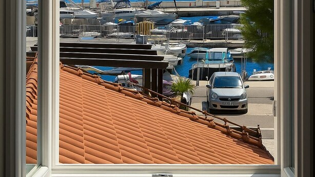 Blick aus einem Fenster auf eine Marina mit vertäuten Booten, einem klaren blauen Himmel und einer hügeligen Landschaft im Hintergrund.