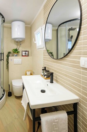 Een badkamer met een witte wastafel, spiegel, toilet en douche.