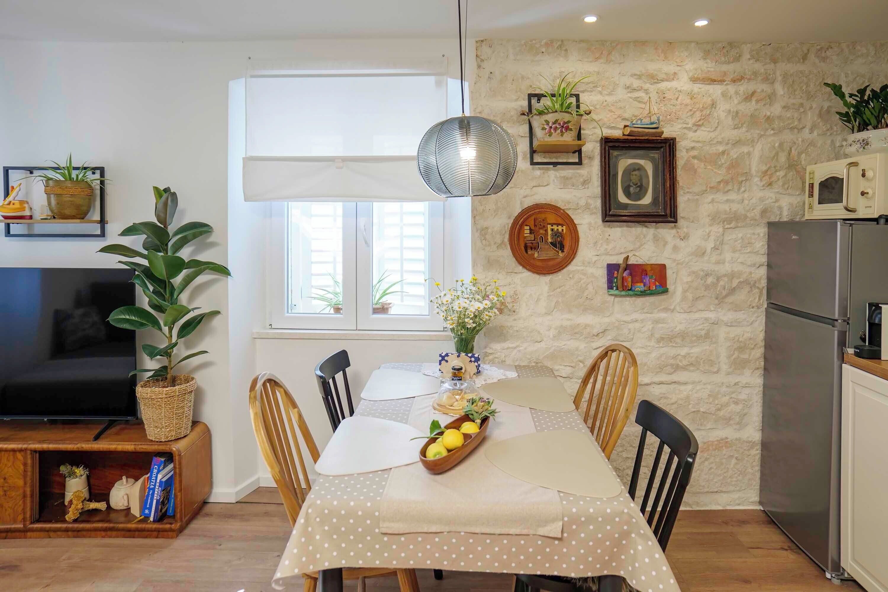 Un comedor con una mesa dispuesta para dos, una pared de piedra y una zona de cocina con electrodomésticos.