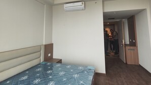 A bedroom with a bed, a ceiling fan, an air conditioning unit, and a wooden wardrobe. - Khatu Hotel (Greater Noida)