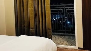 A hotel room with a bed, a window with curtains, and a view of the outside at night. - Khatu Hotel (Greater Noida)