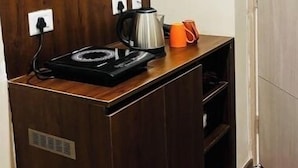 A small kitchenette with a wooden countertop, a kettle, a mug, and a power outlet. - Khatu Hotel (Greater Noida)