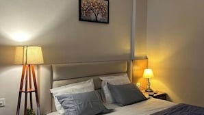 A bedroom with a bed, two bedside lamps, a wall-mounted air conditioner, and a framed picture. - Khatu Hotel (Greater Noida)