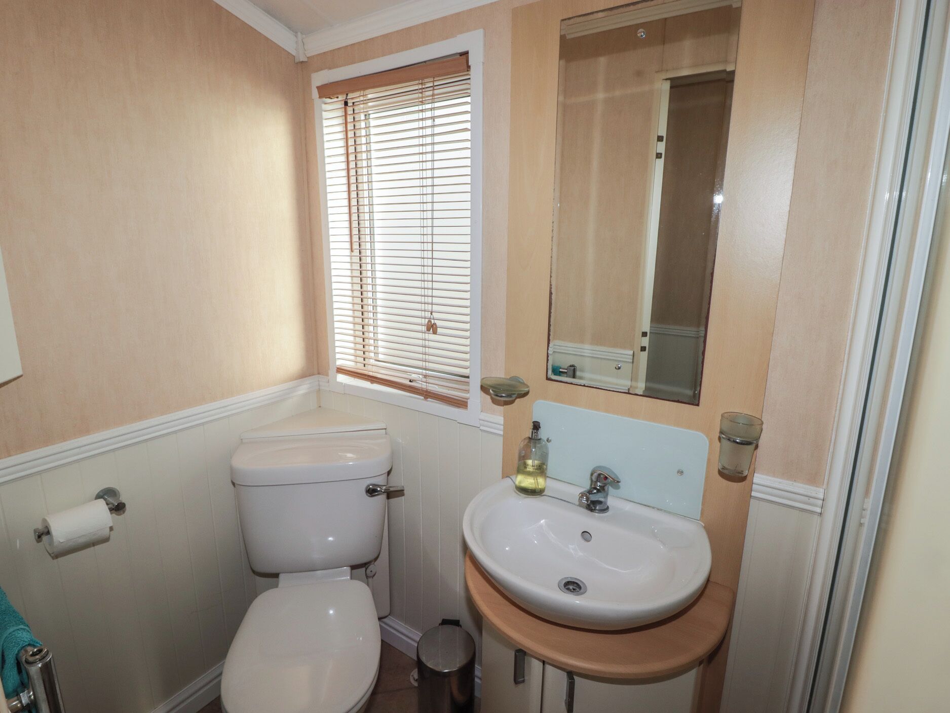 A small bathroom with a toilet, sink, and window with blinds.