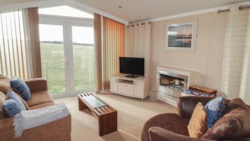 A spacious living room with a television, fireplace, and a view of a grassy field through large windows.