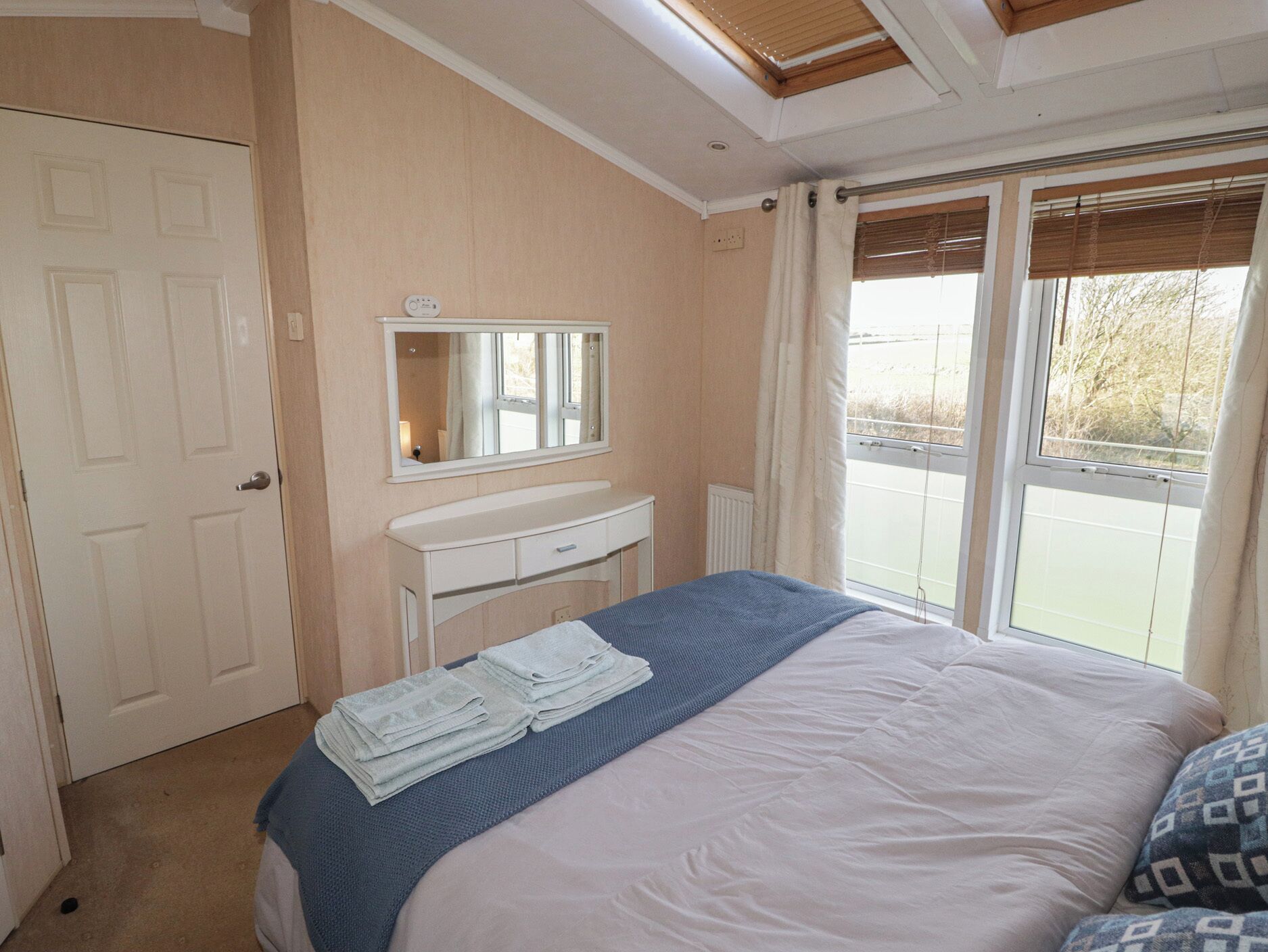 Ein Schlafzimmer mit einem Bett, einem Schminktisch, einem Spiegel und einem Fenster mit Vorhängen.