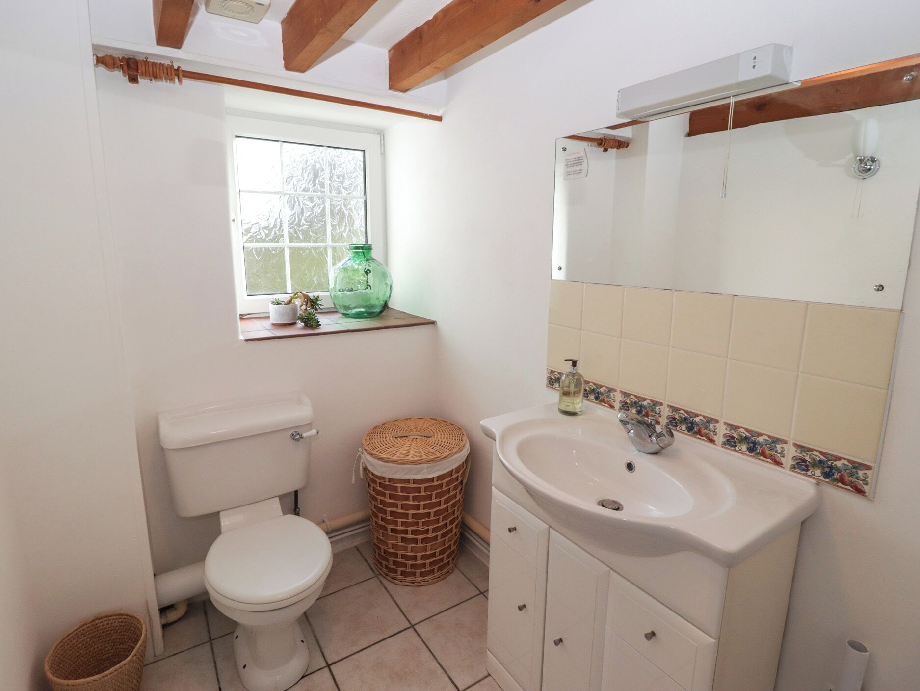 Een kleine badkamer met een toilet, een wastafel, een raam en een spiegel.