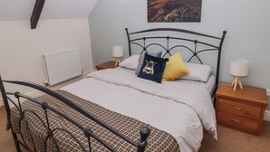 Quarto com cama, duas mesas de cabeceira, radiador, quadro na parede e teto inclinado.