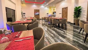 A modern dining area with marble flooring, red and beige chairs, and tables set with cutlery and napkins. - Lavilla Apartment (Abuja)