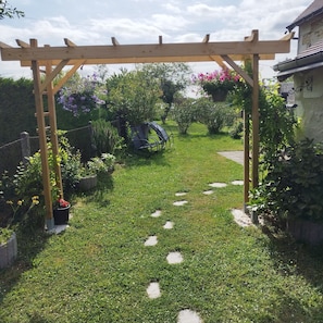 Un jardín con un pérgola de madera, piedras para caminar y diversas plantas.