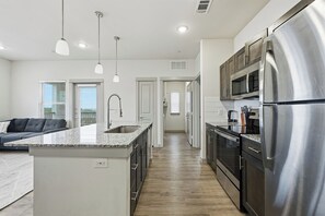 Une cuisine moderne dotée d’appareils électroménagers en acier inoxydable, d’un îlot central, de luminaires suspendus et donnant sur un espace de vie.