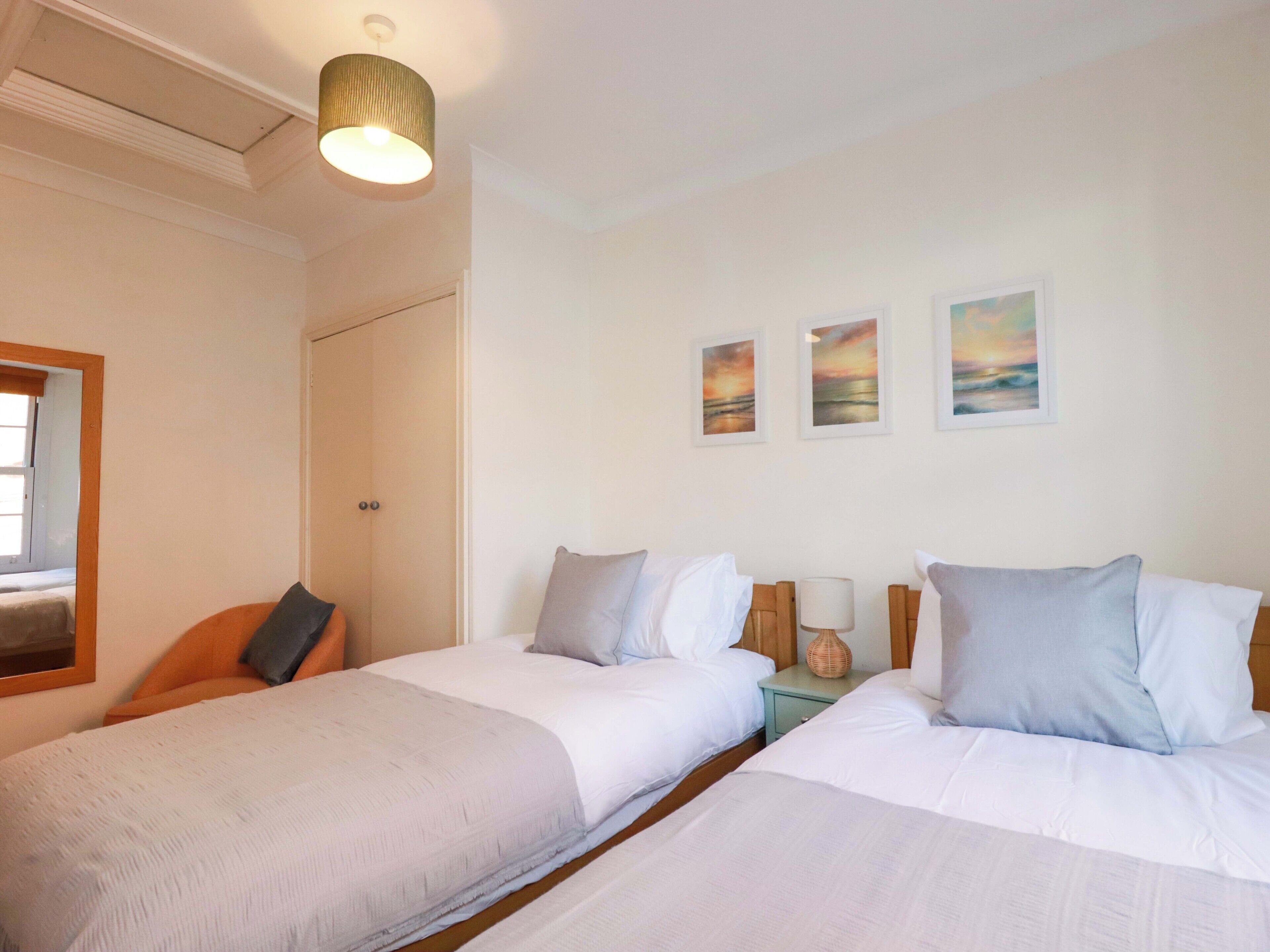 A hotel room with two beds, a nightstand, a lamp, and three framed pictures on the wall.