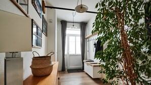 A narrow hallway with a wooden floor, a woven basket, a hanging plant, and a door leading to a bright room. - Unique Carpenter’s Apartment with Sea View, Balcony, and Wi-Fi (Oldenburg)