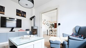 A modern living room with a flat-screen TV, a glass coffee table, a blue armchair, and a fireplace. - Unique Carpenter’s Apartment with Sea View, Balcony, and Wi-Fi (Oldenburg)