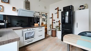 A modern kitchen with white cabinetry, a built-in oven, a stainless steel range hood, and a black refrigerator. - Unique Carpenter’s Apartment with Sea View, Balcony, and Wi-Fi (Oldenburg)