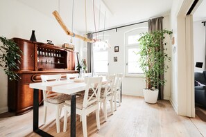 A dining area with a wooden bar, white chairs, a white table, and a potted plant. - Unique Carpenter’s Apartment with Sea View, Balcony, and Wi-Fi (Oldenburg)