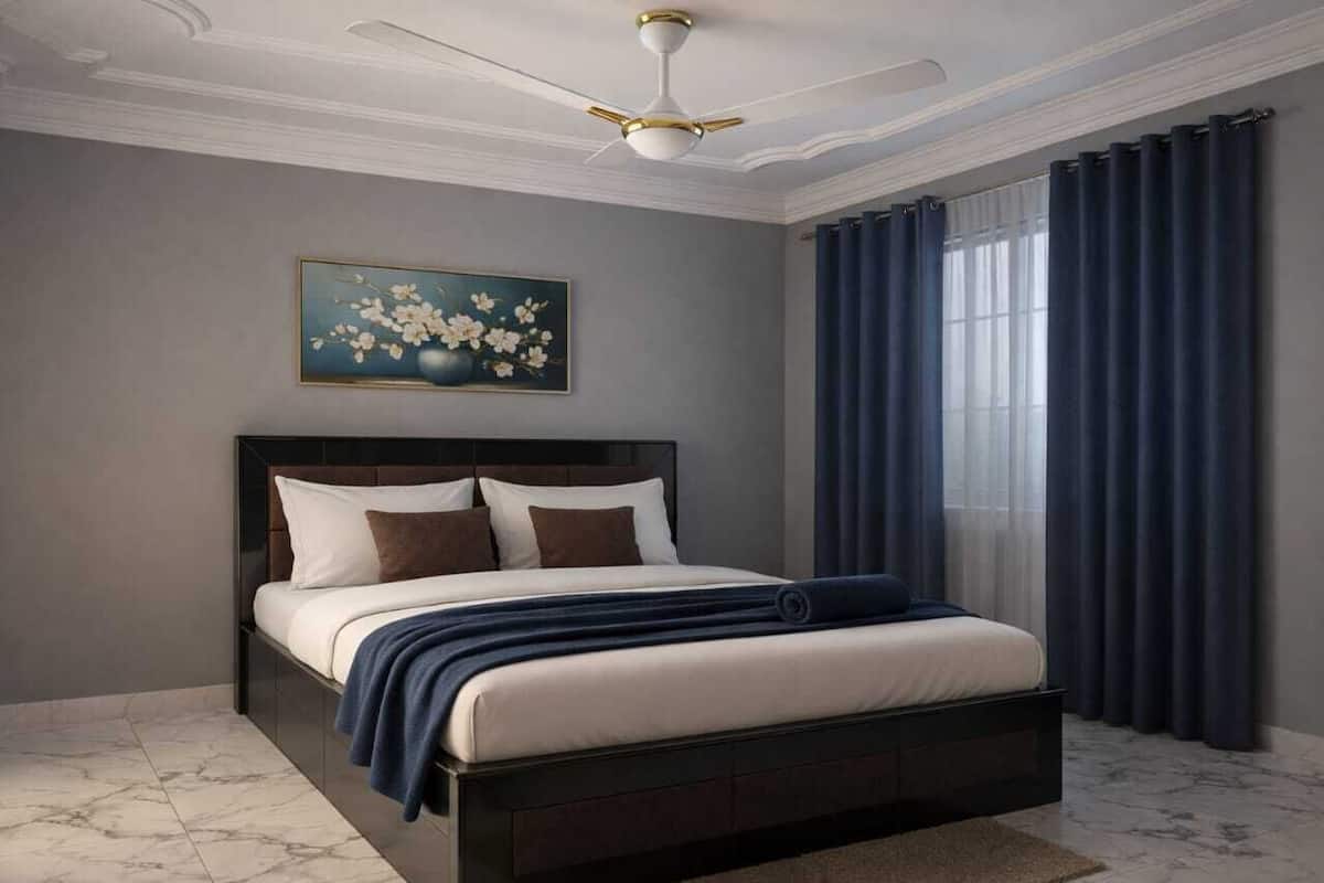 Een slaapkamer met een bed, plafondventilator, schilderij en gordijnen.