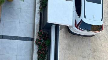 Um carro branco estacionado sobre um piso de azulejos, com um vaso de flores vermelhas e folhagem verde ao lado.