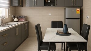 A modern kitchen with dark grey cabinets, a built-in oven, and a dining area with a marble table and black chairs. - Deutsch Inn Luxury Apt (Weija)