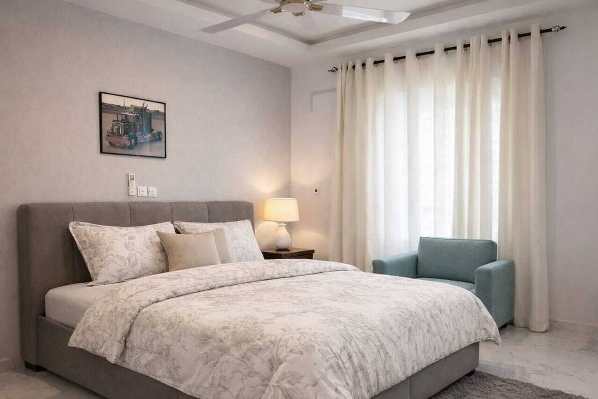 Een moderne slaapkamer met een groot bed, een nachtkastje, een lamp en een stoel.
