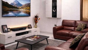 A modern living room with a flat-screen TV, leather sofas, a coffee table, and a cabinet with a decorative item. - Deutsch Inn Luxury Apt (Weija)