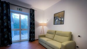 A living room with a sofa, a floor lamp, a painting, and a sliding glass door leading to an outdoor area. - Valle dei Casali (Rome)