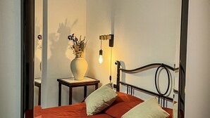 A bed with a red bedspread and two pillows, a bedside table with a vase and a lamp, and a wall-mounted mirror reflecting the room. - Valle dei Casali (Rome)