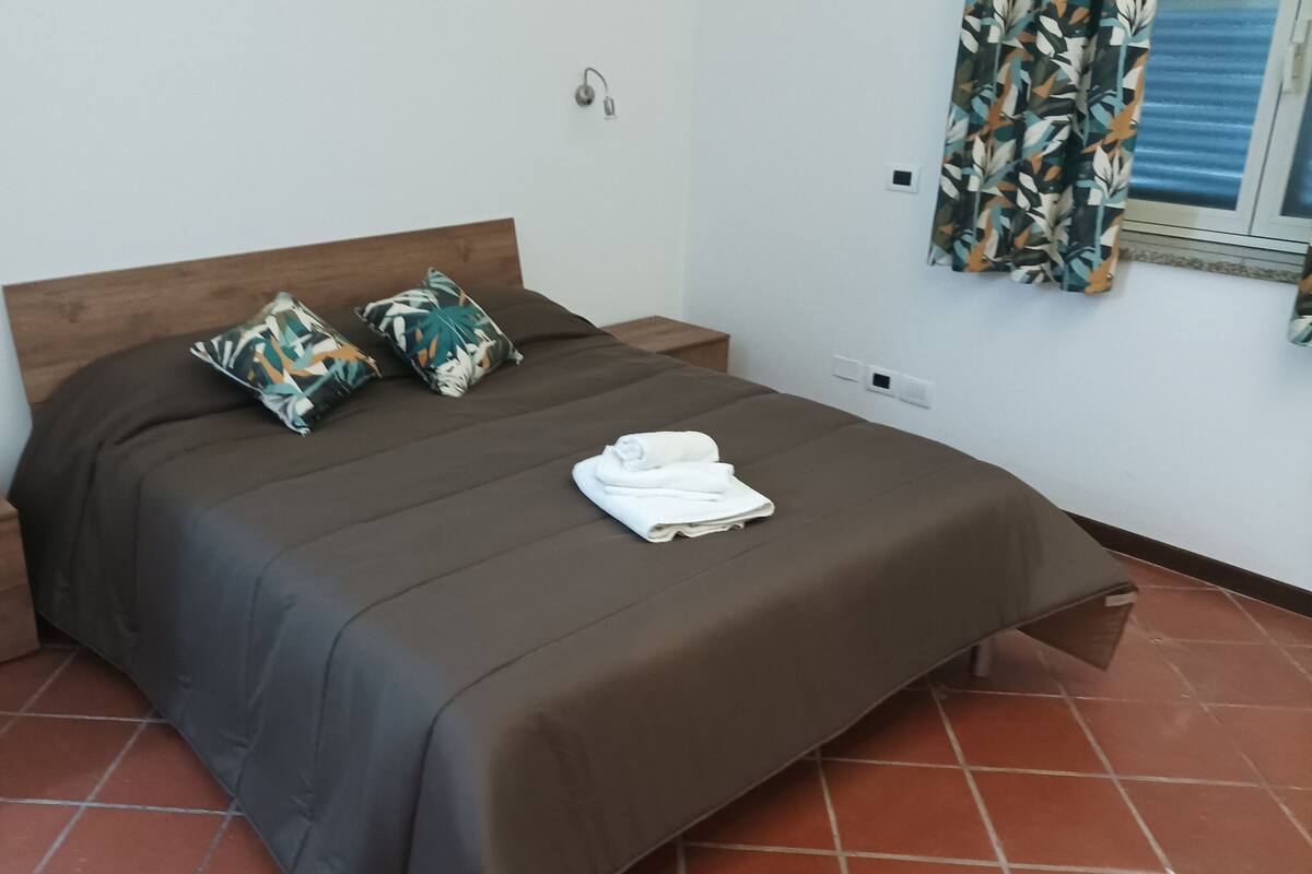 Un lit bien fait, recouvert d’une couverture marron, avec deux coussins à motifs et une serviette blanche pliée posée sur le lit.