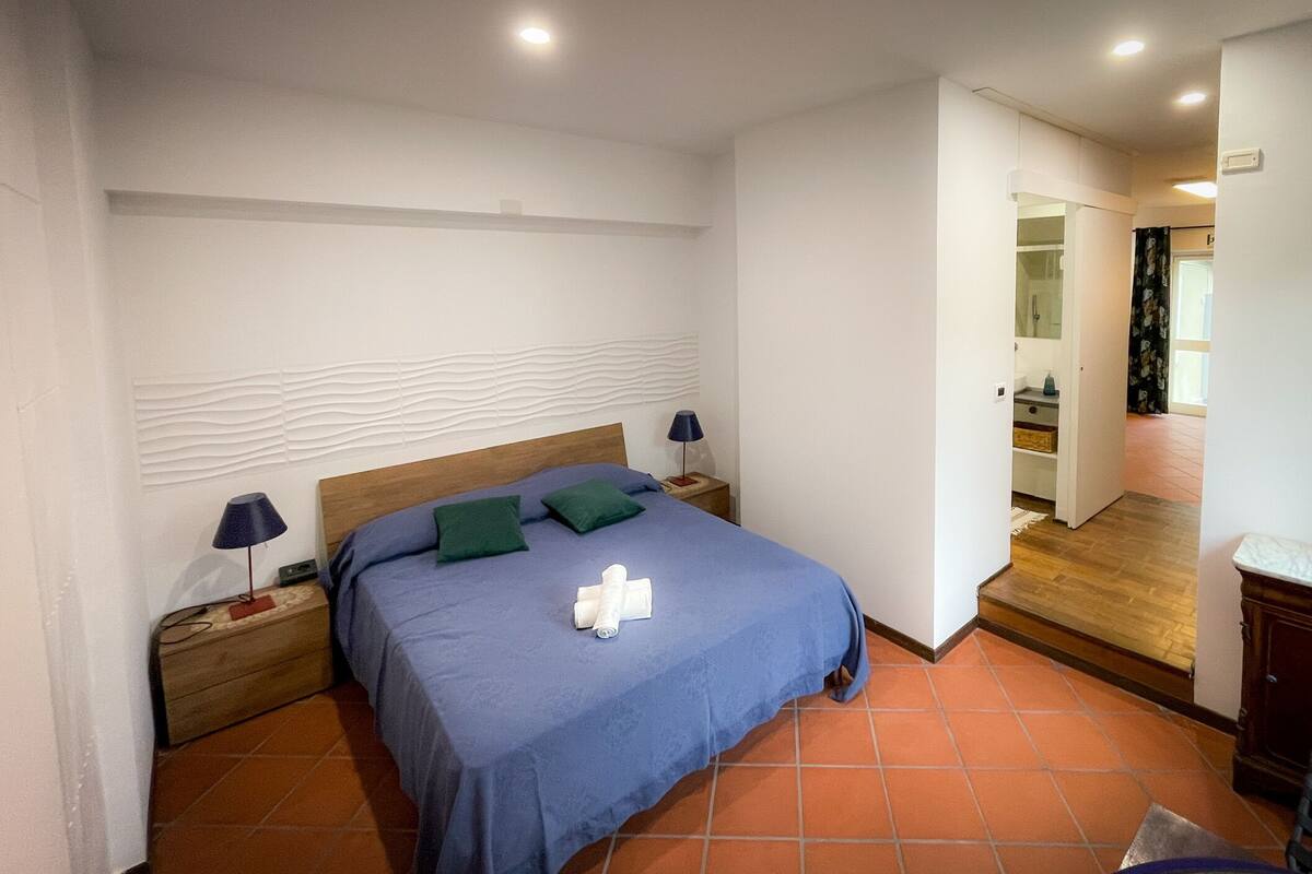 Une chambre à coucher comprenant un lit, deux tables de chevet, une commode, une commode en bois et une salle de bain visible à travers une porte ouverte.
