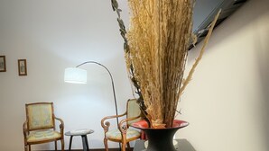 A room with a large vase of dried plants on a table, two chairs, a small table with a lamp, and a patterned rug. - Valle dei Casali (Rome)