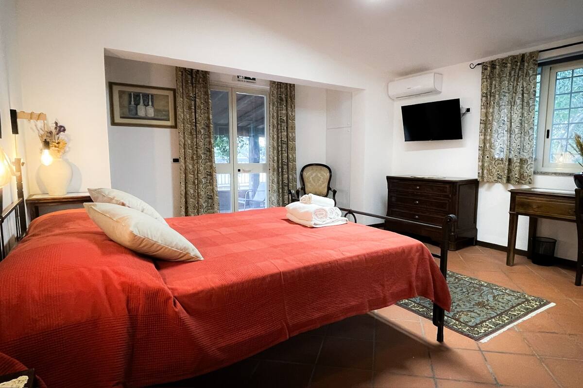 Une chambre d’hôtel avec un grand lit, un bureau, une chaise, une télévision et une fenêtre avec des rideaux.