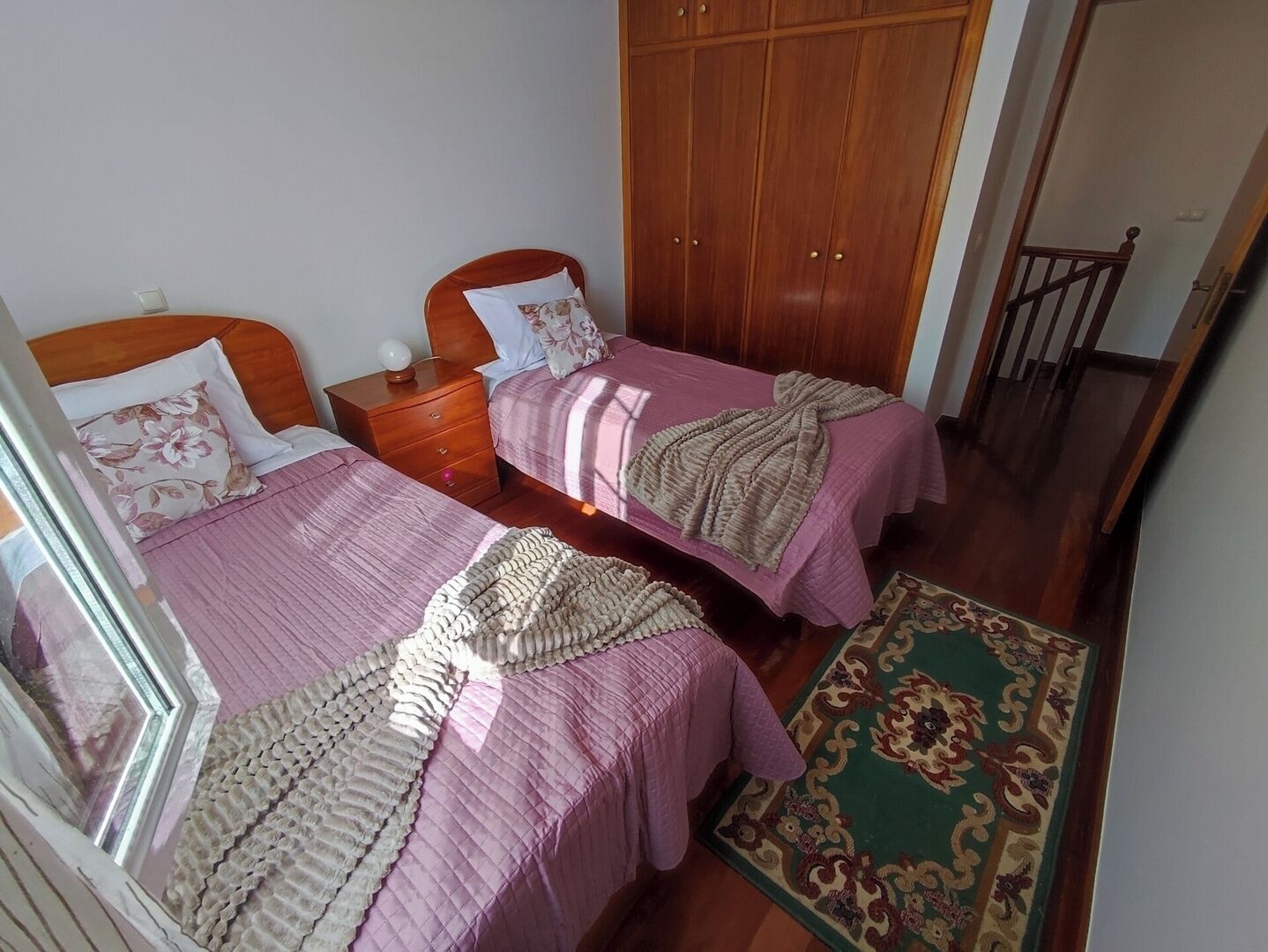 Een kamer met twee bedden, een houten garderobe en een tapijt met een groen patroon.