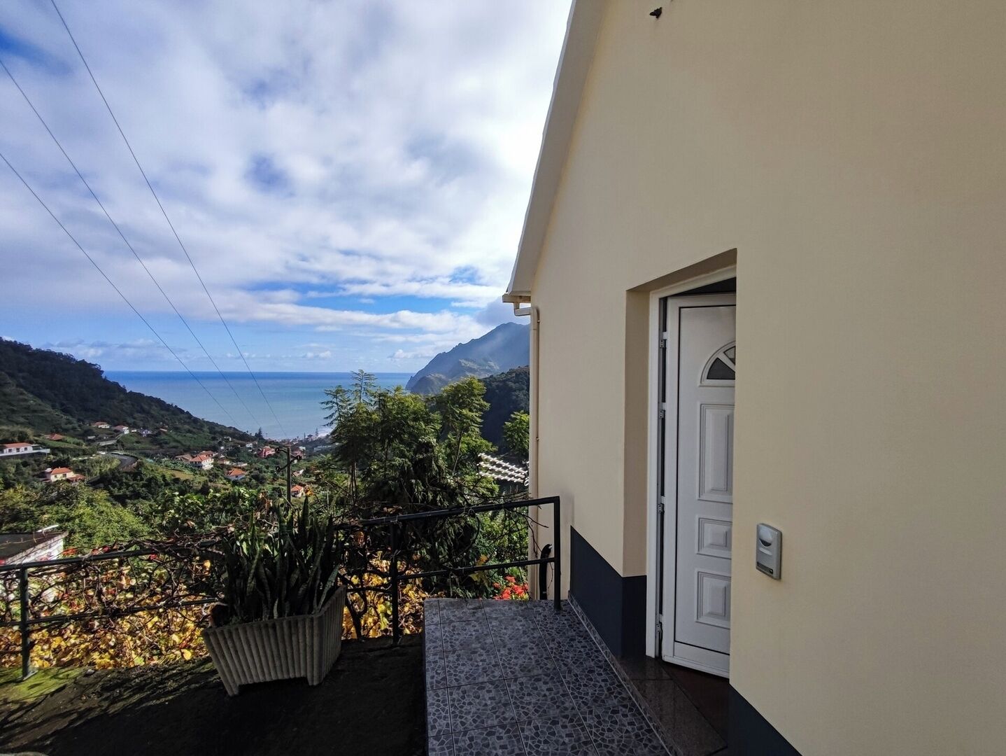 Un balcon donnant sur un paysage côtier, une porte blanche et un pot de fleurs.