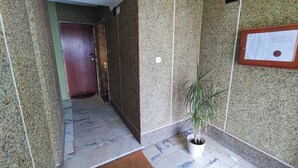 Un corridoio con pavimento in marmo, una pianta in vaso, una porta e un avviso.