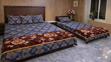 A room with two beds, wooden paneling on the walls, a window with a view, and a vase with flowers on the nightstand.