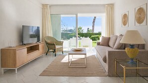 A living room with a TV, sofa, coffee table, and a view of the outdoors. - Sunny Garden Apartment Miraflores (Mijas Costa)