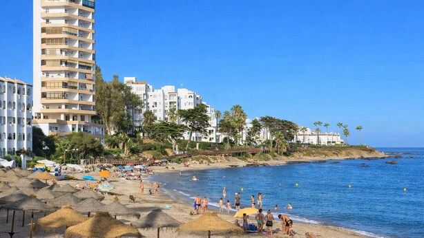 A beach with a tall hotel, palm trees, and umbrellas. - Sunny Garden Apartment Miraflores (Mijas Costa)